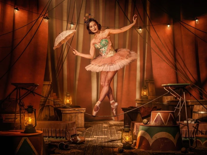 Dancer in a pink tutu and ornate bodice balancing on a tightrope inside a circus tent photographed by Dana Hursey.