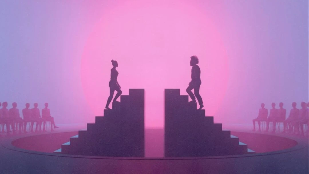 Silhouetted figures ascend stairs on either side of a circle stage, with an audience, against a pink and purple gradient background.