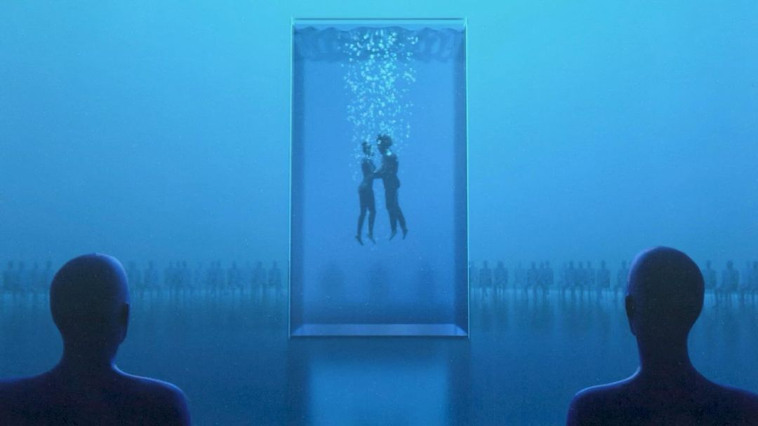 Two people embracing underwater inside a glass tank, observed by silhouetted figures in a monochromatic blue atmosphere, surreal and dreamlike.