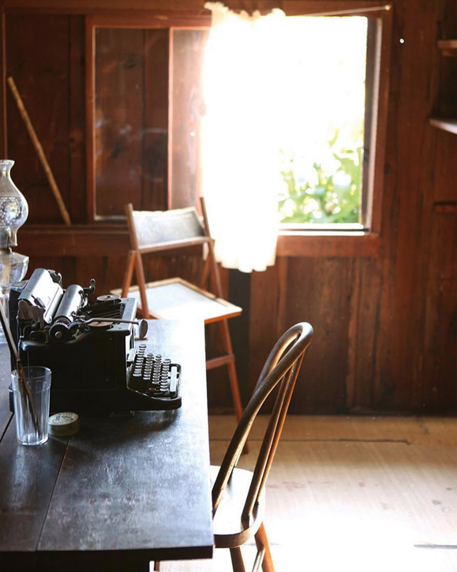 Vintage workspace featuring a dark wood desk, antique typewriter, and classic wooden chair near a window with soft, bright lighting.