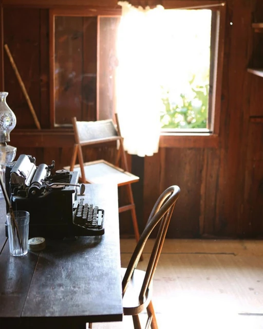 Vintage workspace featuring a dark wood desk, antique typewriter, and classic wooden chair near a window with soft, bright lighting.