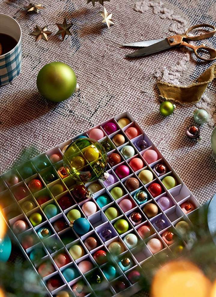 Overhead shot: box of colorful Christmas ornaments, cup, scissors, and star decorations on a textured surface, holiday ambiance.