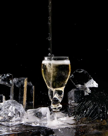 Champagne being poured into a glass surrounded by chunks of ice against a dark background, creating an elegant and refreshing visual.