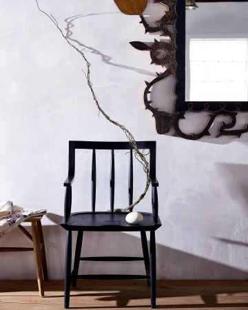 Black wooden chair with a white rock, set against a stark white wall with a decorative mirror, creating a minimalist, artistic composition.