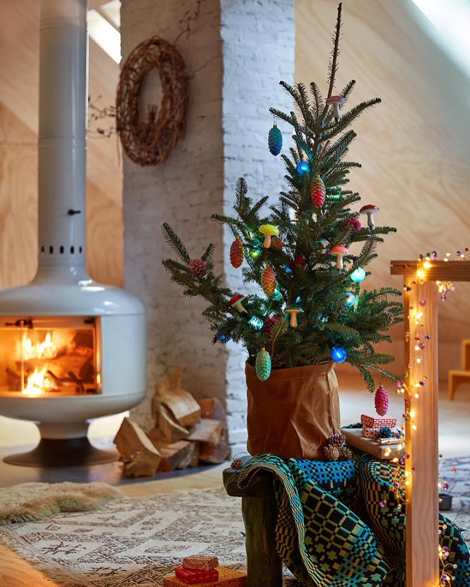 Cozy holiday scene featuring a small decorated Christmas tree in a brown paper bag, set beside a modern white fireplace in a warm, inviting room.