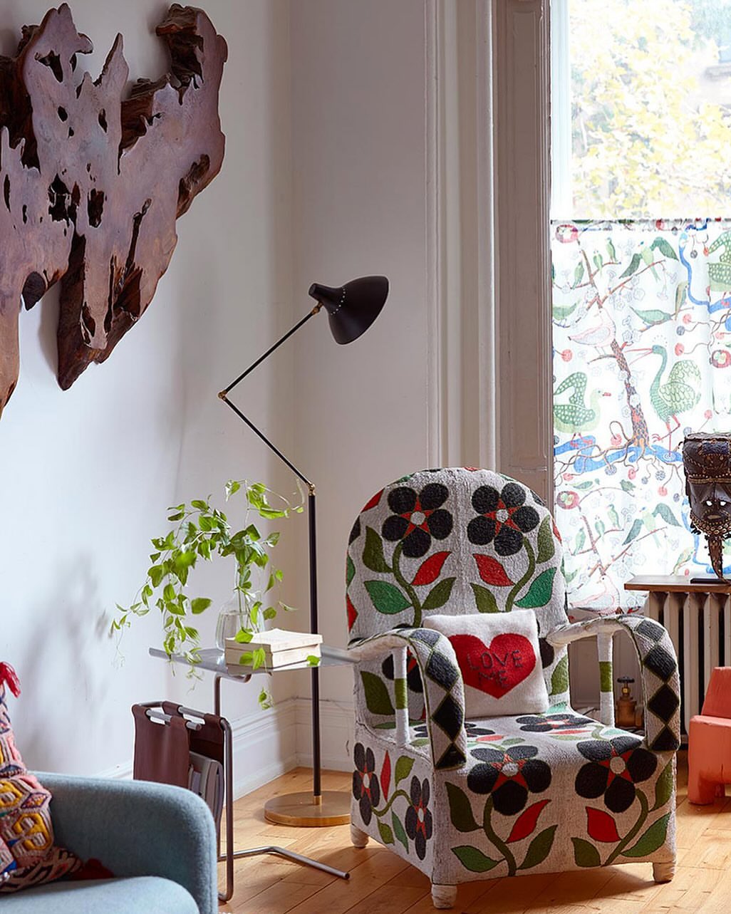 Interior of a living room featuring a floral patterned armchair with a heart-shaped pillow, floor lamp, and various decorative items.