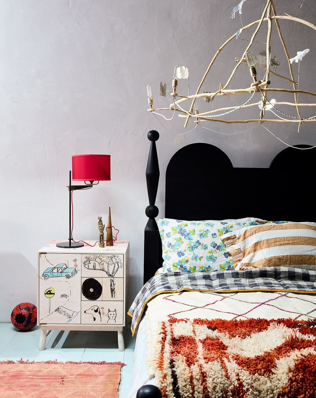 Bedroom interior featuring a bed with patterned bedding, bedside table with lamp and decor, and a whimsical chandelier.