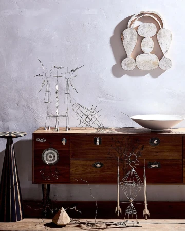 Contemporary art composition featuring geometric wire sculptures, a rustic wooden dresser, white bowl, and a decorative wooden wall hanging.
