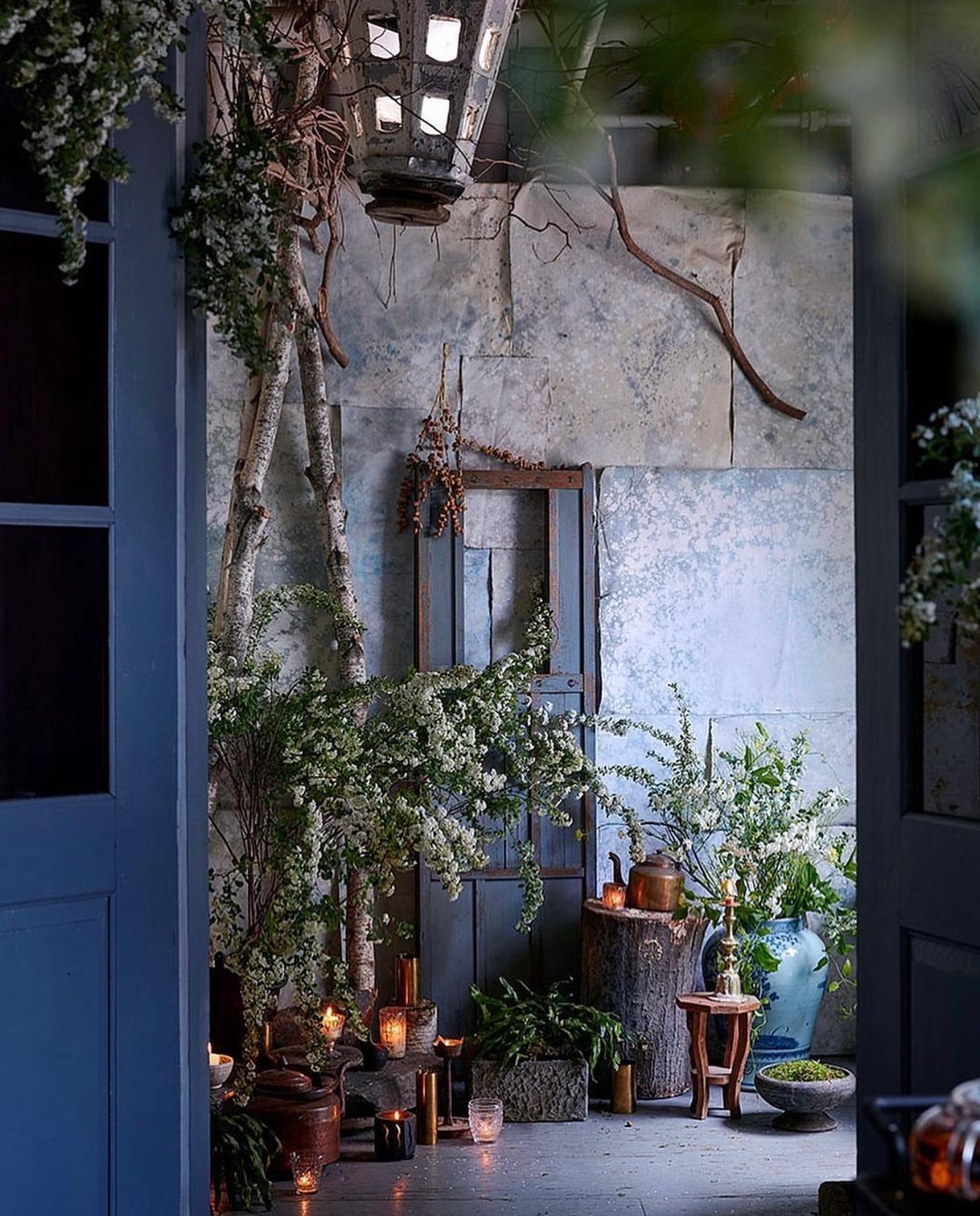 Indoor entryway decorated with candles, greenery, and birch branches; vintage lantern hangs above rustic doorway.