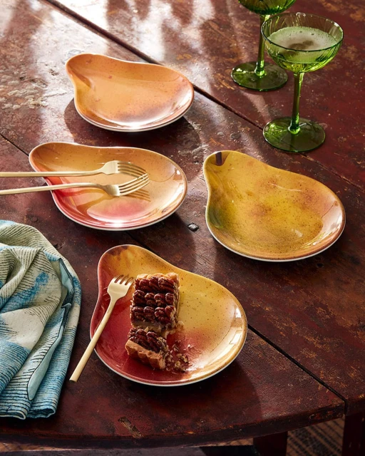 Overhead shot of pear-shaped ceramic plates, gold forks, vintage green glassware, and a patterned napkin on a wooden table.