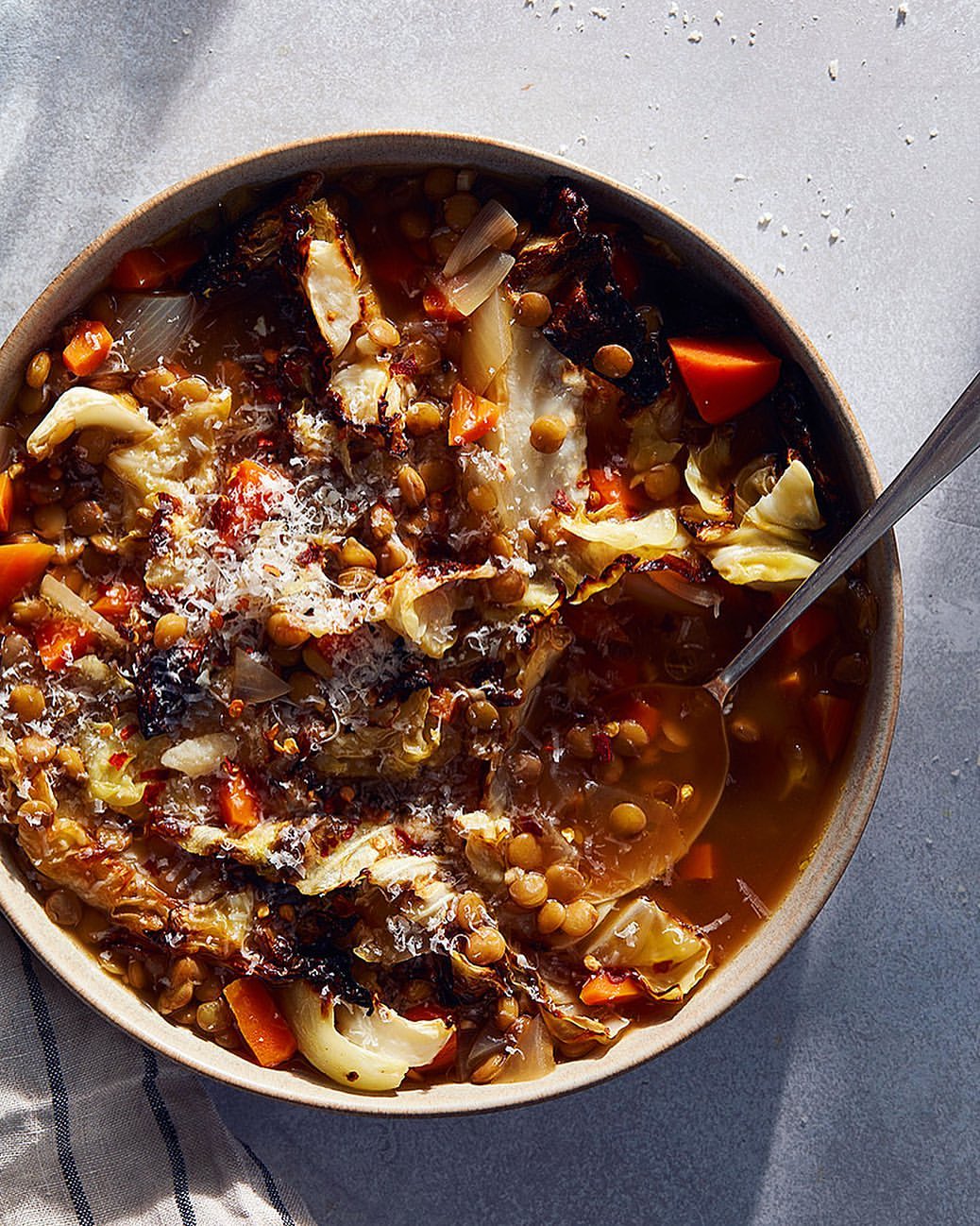Overhead shot of lentil soup in a bowl with carrots, cabbage and onions, topped with cheese and garnished with a spoon on the side.