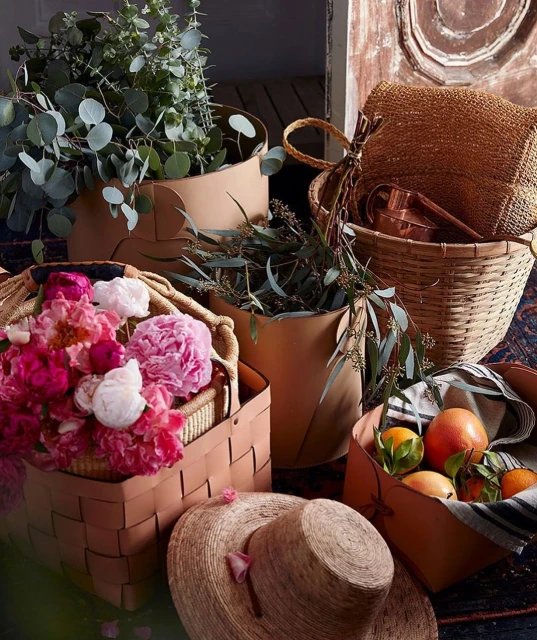 Still life of baskets filled with flowers, greenery, and citrus fruits, showcasing textures and natural tones with warm lighting.