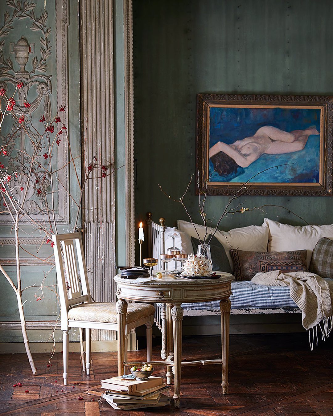 Interior view with round table set with glasses, antique chair, and framed painting of nude figure; olive green wall and wood floors.