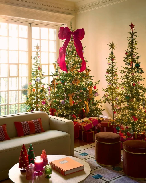 Living room with four decorated Christmas trees, wrapped gifts, a sofa, stools, and a round table with decorative objects.