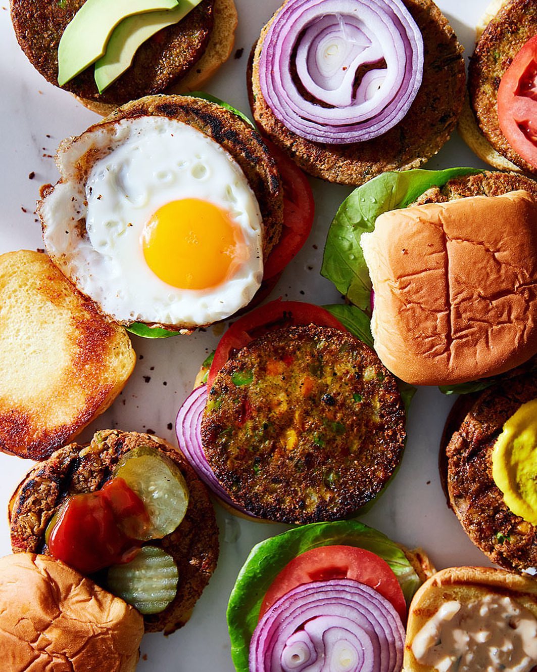Overhead shot of veggie burgers assembled with an egg, avocado, red onion, tomato, lettuce, pickles, ketchup, and mayonnaise.
