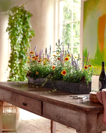 Long rectangular planter filled with wildflowers and purple blooms centered on a rustic wooden table indoors