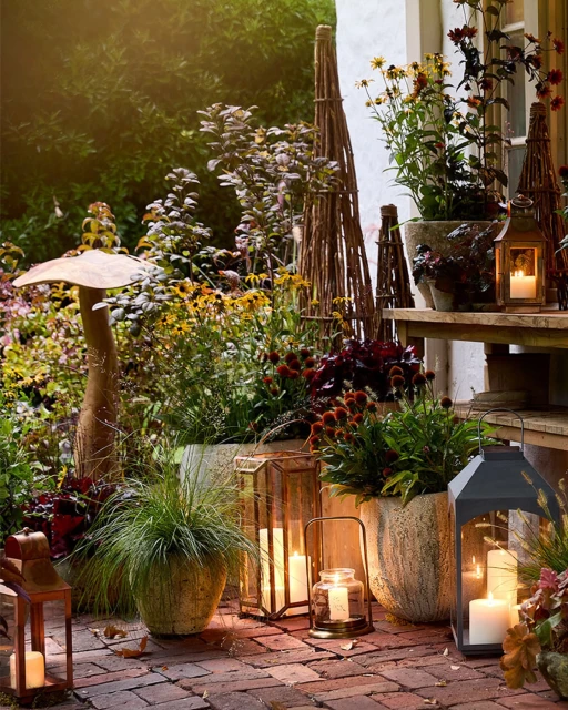 Outdoor garden scene with glowing lanterns, potted plants, and brick pathway creating a warm, inviting ambiance at dusk.