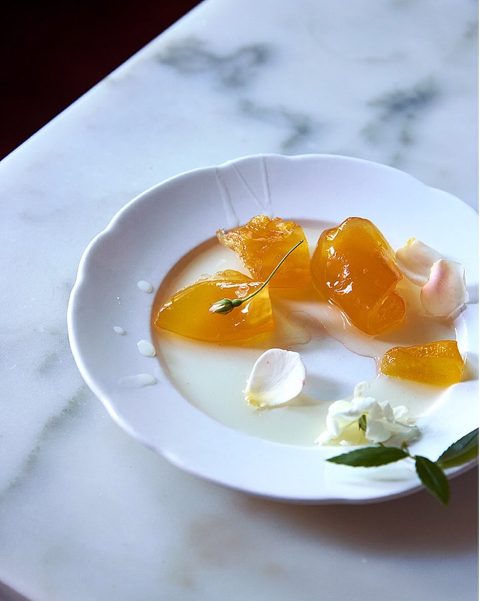 Delicate white plate showcasing golden fruit preserves and fresh white flower petals on a marble surface, capturing elegant food presentation.