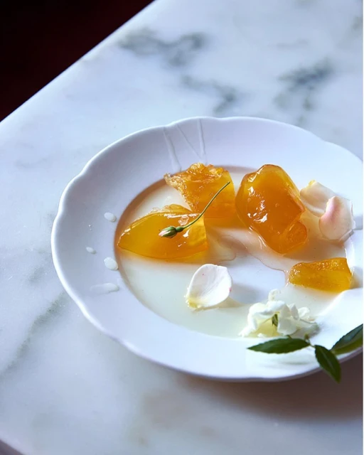 Delicate white plate showcasing golden fruit preserves and fresh white flower petals on a marble surface, capturing elegant food presentation.