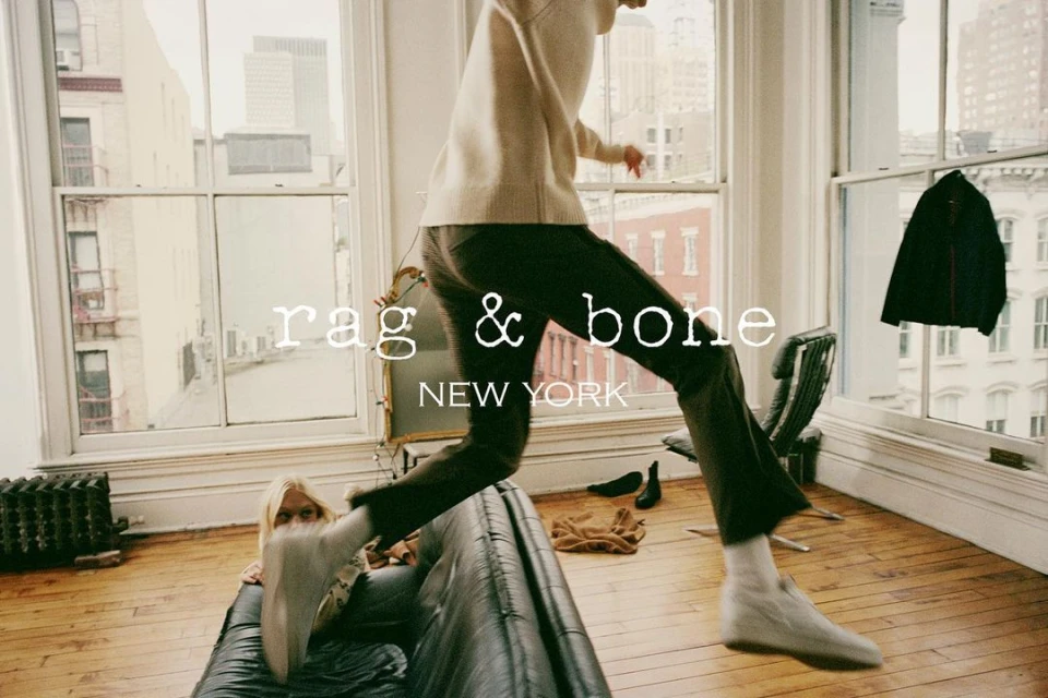 Fashion editorial shot of a man jumping over a black leather sofa in a loft apartment, with a woman sitting on the sofa.