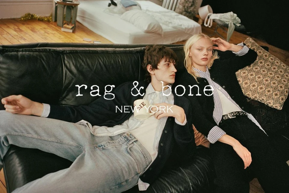 Fashion ad featuring a casually posed couple on a black leather sofa, with the 'rag & bone NEW YORK' logo prominently displayed.