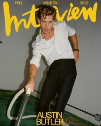 Actor Austin Butler vacuuming in a white shirt and black trousers against a neutral wall by photographer Daniel Arnold