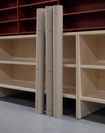 Three cardboard tubes stand upright against light-colored shelving, with a burgundy shelving unit in the background against a gray floor.