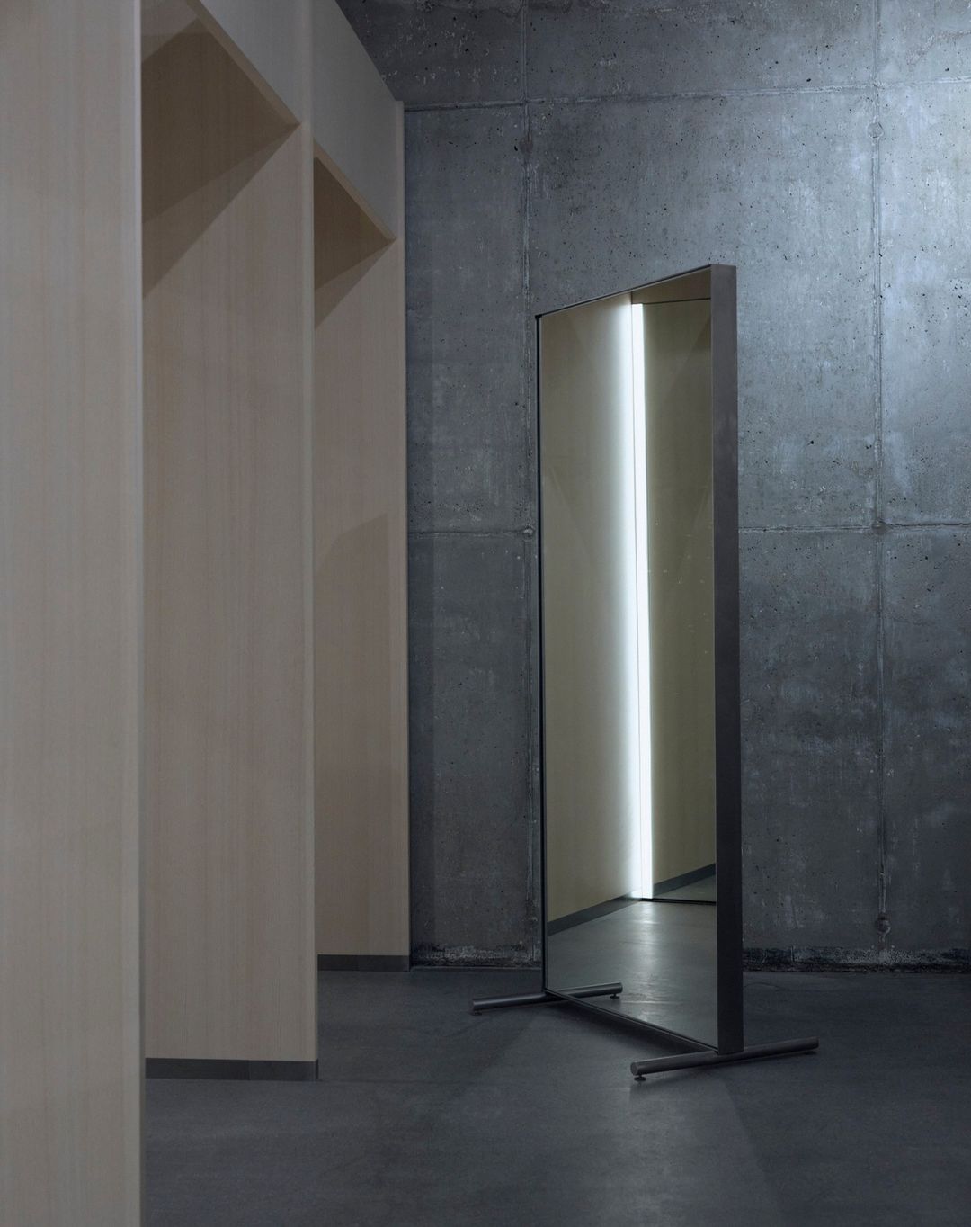 Modern interior featuring a full-length mirror with a metal frame against a textured concrete wall, reflecting a bright light source.