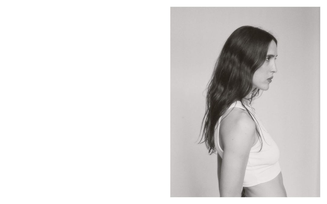 Profile shot of an adult woman with dark hair and a white top, set against a plain studio backdrop and captured in monochrome.