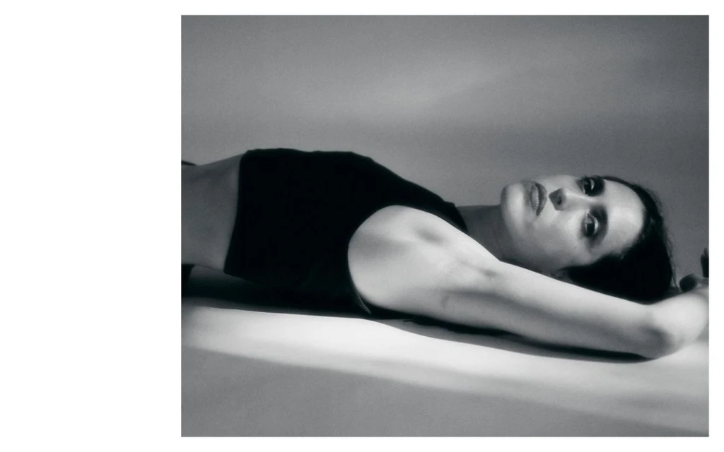 Monochrome portrait of a woman lying down with her arms above her head, soft lighting, and a contemplative facial expression.