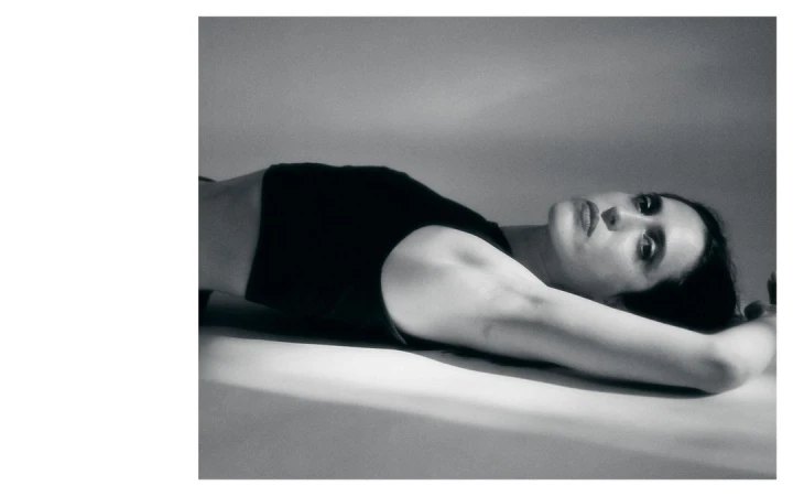 Monochrome portrait of a woman lying down with her arms above her head, soft lighting, and a contemplative facial expression.