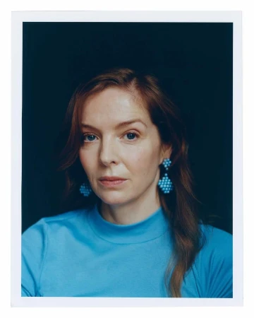 Portrait of a redhead woman wearing blue earrings and a matching top against a dark background, showcasing beauty and fashion.