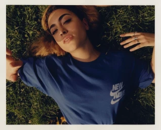 Woman wearing a blue t-shirt lying on green grass captured in a polaroid frame