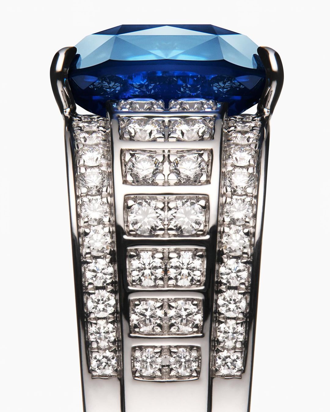 Close-up of a platinum ring with large cushion-cut blue gemstone and pave diamonds, showcasing luxury jewelry design on white backdrop.