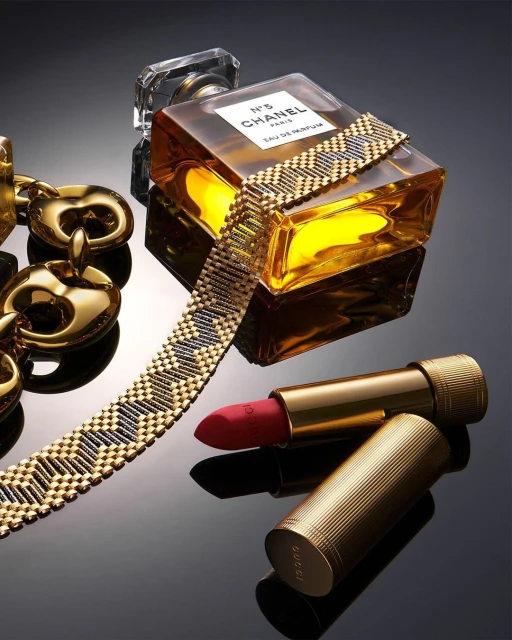 Still life shot of a Chanel perfume bottle, Gucci lipstick, and gold chain on a glossy black surface, product photography, studio lighting.