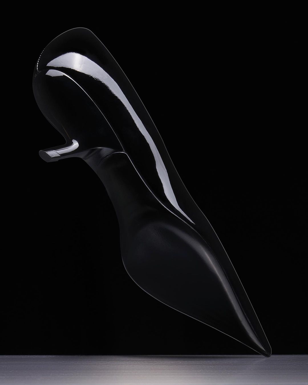 Elegant black high-heeled shoe on reflective surface against a dark backdrop, showcasing fashion footwear in a studio setting.
