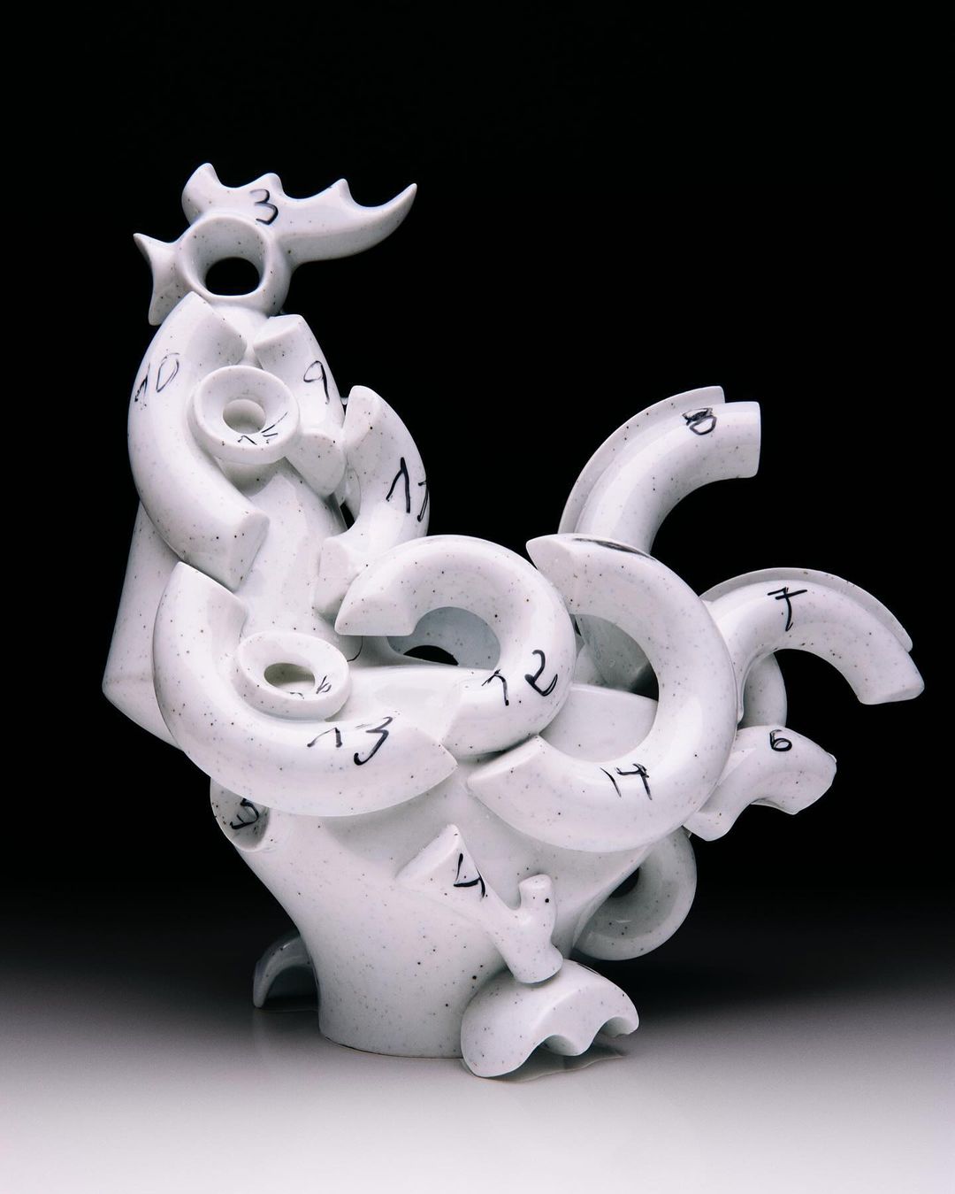 Sculpture of abstract figure with numbers against a dark background. The off-white object features a complex design with circular shapes.