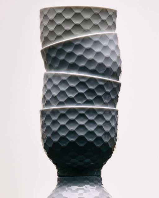 Stack of four gray textured ceramic bowls with footed bases against a white background with reflective surface for commercial use.
