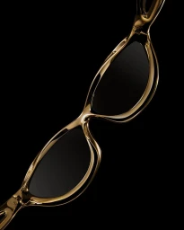 Close-up of polished gold sunglasses with dark tinted lenses against a deep black background, captured diagonally.