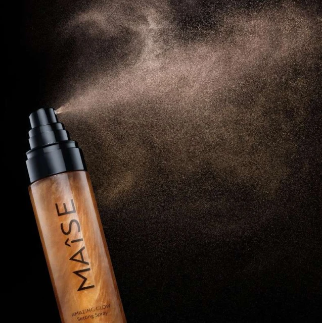 Maise Amazing Glow Setting Spray is shown spraying a fine mist against a dark backdrop, highlighting the radiant effect of the product.
