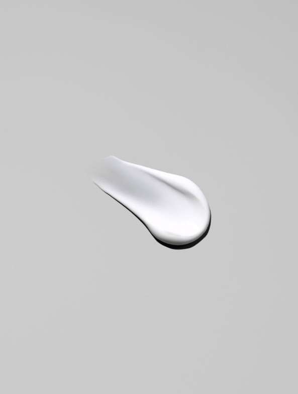 Close-up of a smear of white cream against a neutral gray background, showcasing its smooth texture and reflective surface.