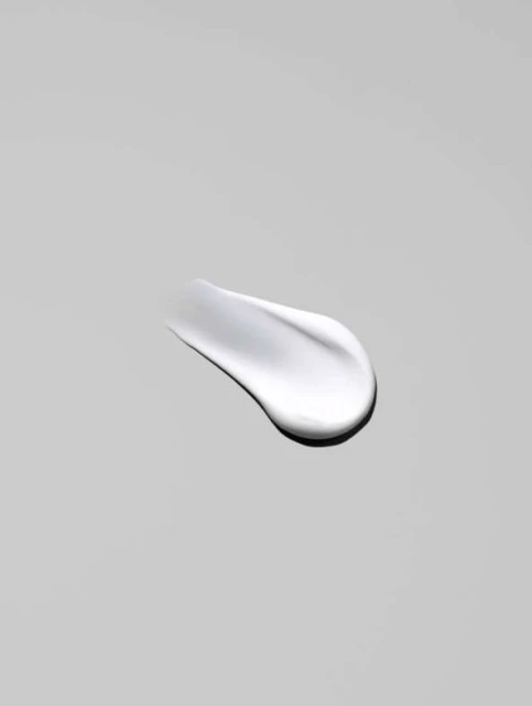 Close-up of a smear of white cream against a neutral gray background, showcasing its smooth texture and reflective surface.