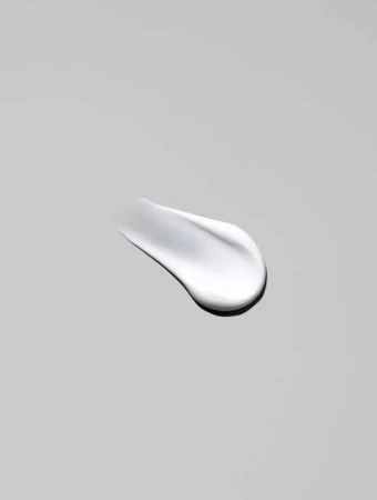 Close-up of a smear of white cream against a neutral gray background, showcasing its smooth texture and reflective surface.