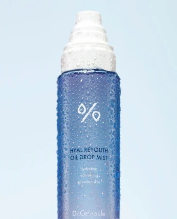 Close-up of a blue and white bottle of Hyal Reyouth Oil Drop Mist skincare product with water droplets against a light blue background.