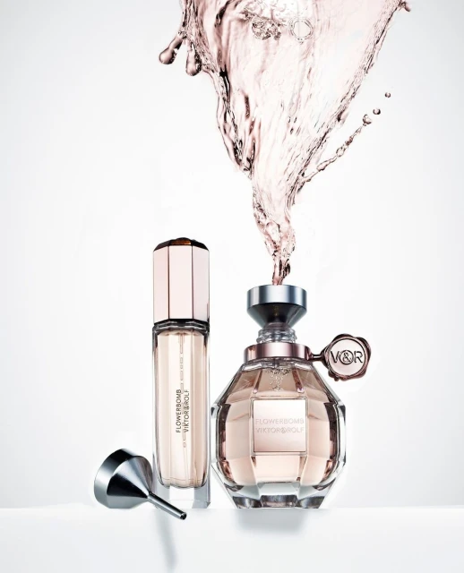 Two perfume bottles, a funnel, and splashing liquid on a white background. The Viktor & Rolf Flowerbomb perfume is a light pink color.