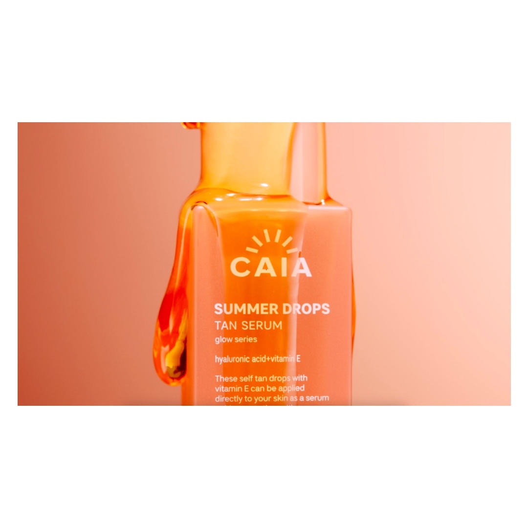 Close-up of a CAIA Summer Drops Tan Serum bottle, showcasing its glossy texture and minimalist design against a peach-toned background.