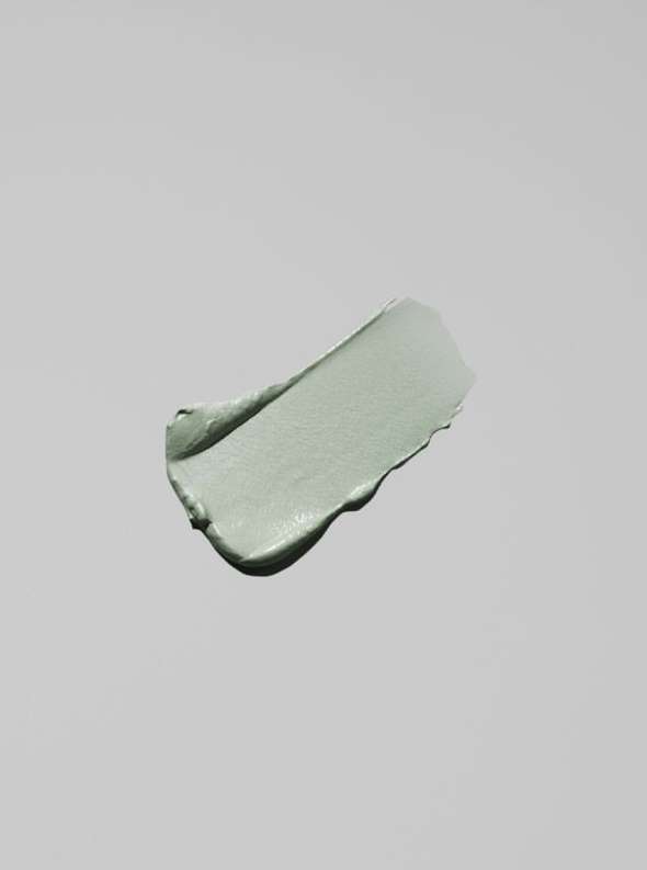 Close-up of a smear of light green clay-based beauty mask on a light gray background with soft lighting and a minimalist aesthetic.