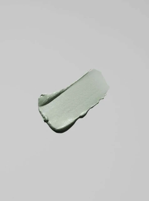 Close-up of a smear of light green clay-based beauty mask on a light gray background with soft lighting and a minimalist aesthetic.