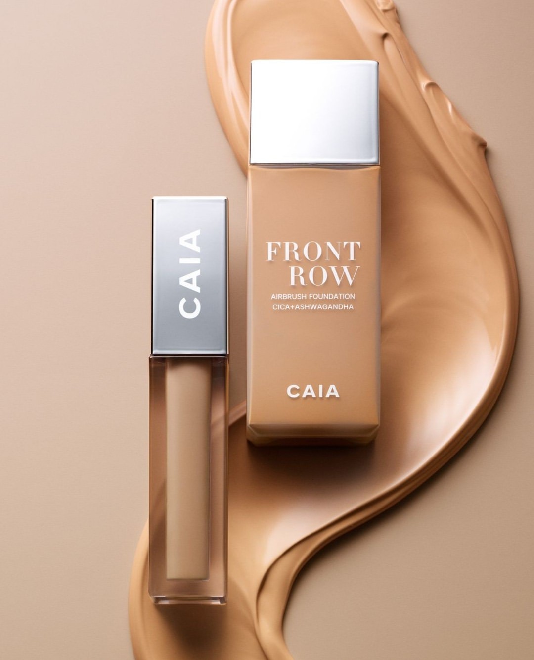 Two bottles of Caia Front Row airbrush foundation and concealer are displayed on a neutral background with a smear of foundation.