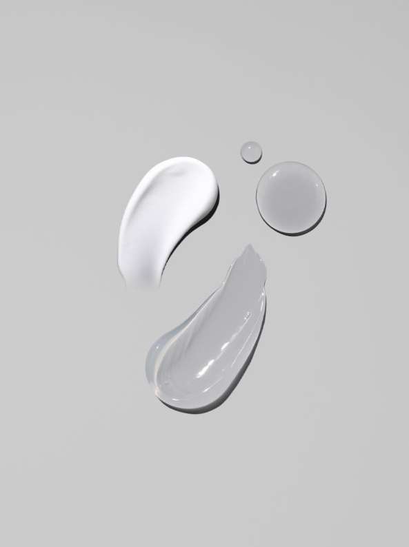 Swatches of facial cream in white and gray tones, along with two water droplets, showcased against a soft gray backdrop.